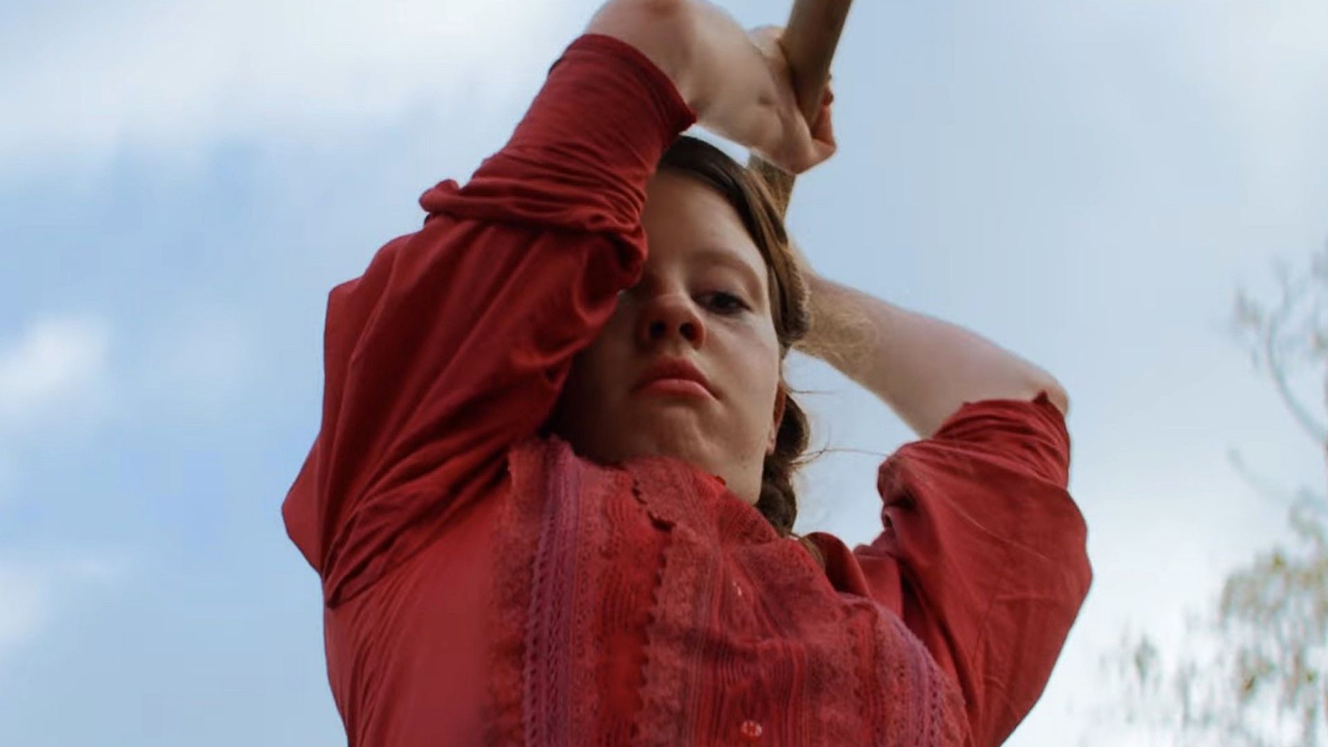 Mia Goth con vestido rojo y una hacha 